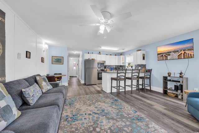 living room featuring wood finished floors, a ceiling fan, and baseboards