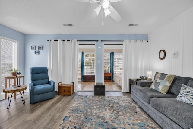 living area with a ceiling fan, visible vents, and wood finished floors