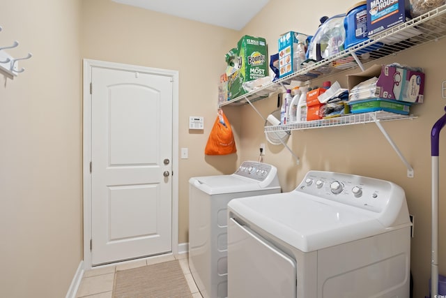 clothes washing area with light tile patterned floors, laundry area, washer and dryer, and baseboards