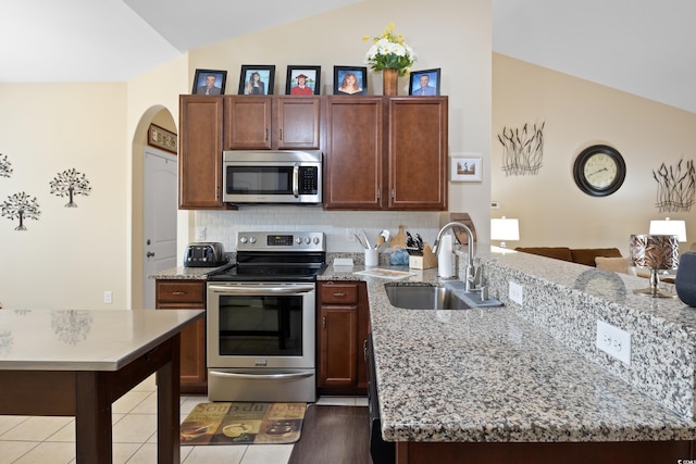 kitchen featuring vaulted ceiling, light stone countertops, stainless steel appliances, and a sink