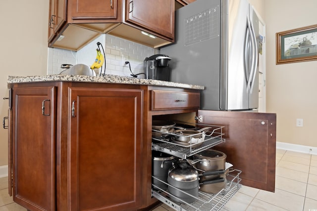 kitchen featuring backsplash, baseboards, light stone counters, stainless steel refrigerator with ice dispenser, and light tile patterned flooring