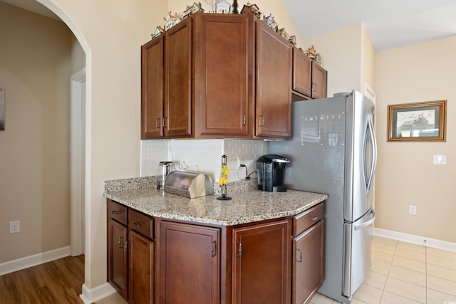 kitchen featuring light stone countertops, baseboards, arched walkways, freestanding refrigerator, and tasteful backsplash