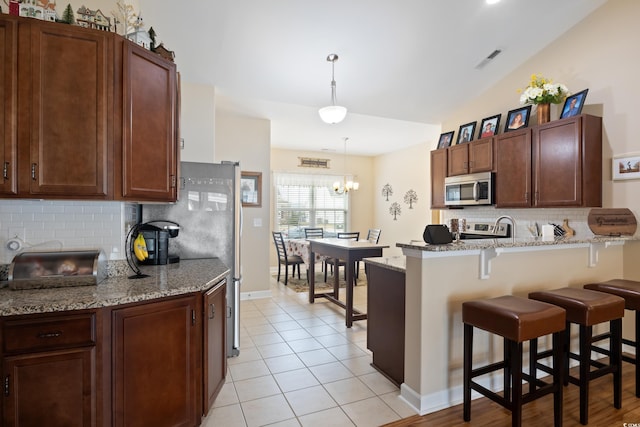 kitchen featuring light tile patterned floors, a peninsula, stainless steel appliances, pendant lighting, and a kitchen bar