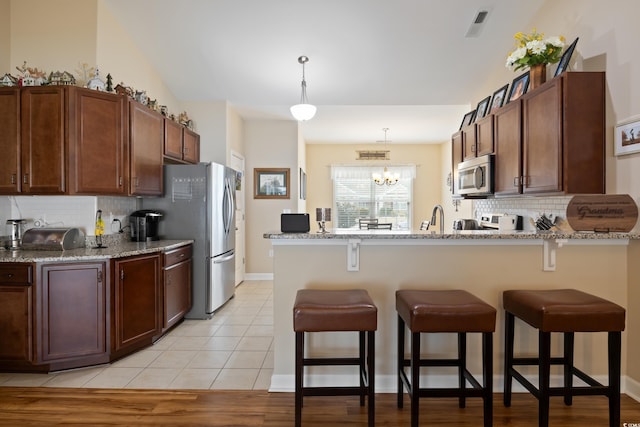 kitchen featuring visible vents, a breakfast bar, light stone counters, light tile patterned floors, and stainless steel appliances