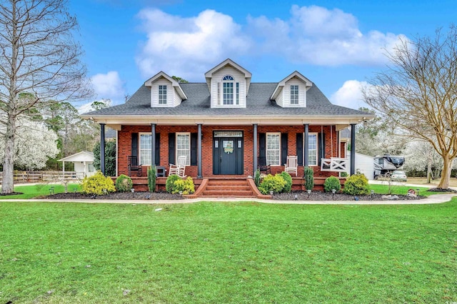 view of front facade featuring covered porch, brick siding, a front yard, and a shingled roof