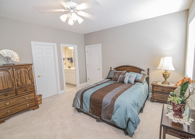 bedroom featuring ensuite bathroom, a ceiling fan, light carpet, a textured ceiling, and baseboards