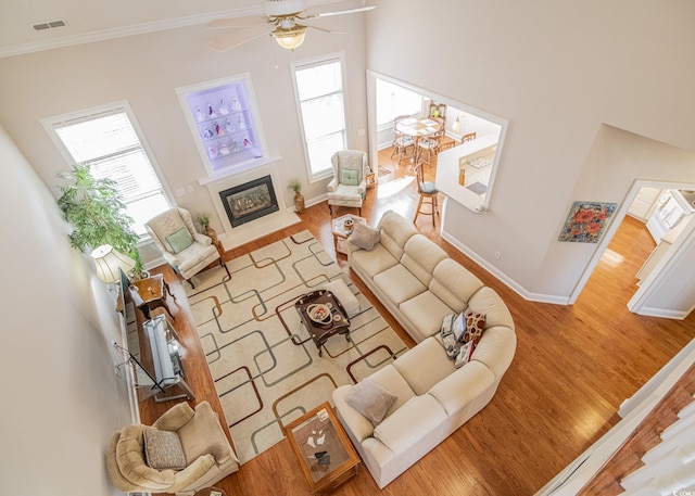 living area featuring crown molding, visible vents, a glass covered fireplace, wood finished floors, and baseboards