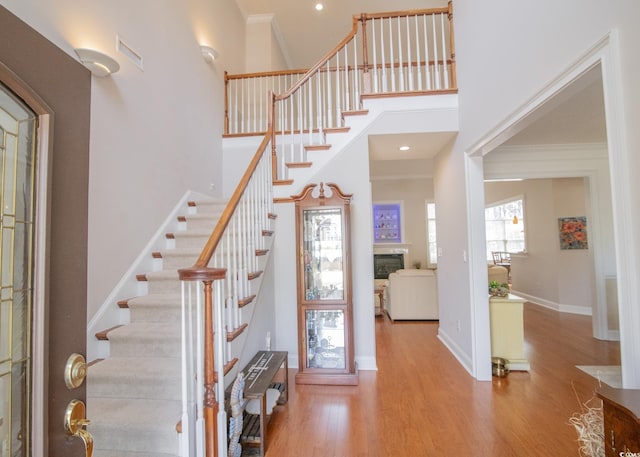 entryway featuring a high ceiling, wood finished floors, baseboards, ornamental molding, and a glass covered fireplace