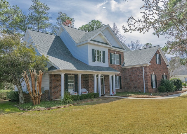 traditional home featuring a shingled roof, a front yard, brick siding, and a porch