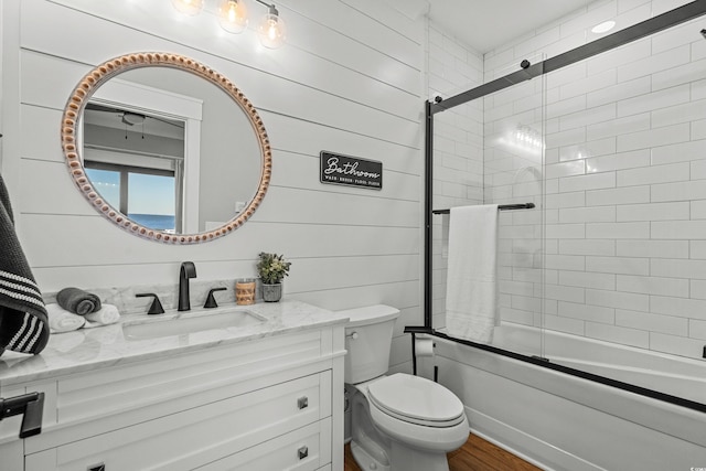 bathroom with toilet, wood finished floors, combined bath / shower with glass door, vanity, and wood walls