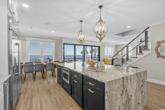 kitchen with built in appliances, a notable chandelier, dark cabinets, ornamental molding, and light wood finished floors