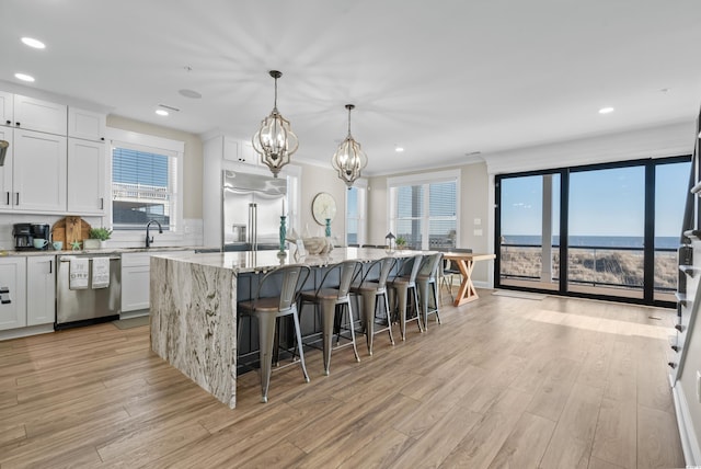 kitchen with white cabinets, an island with sink, light stone counters, a breakfast bar, and stainless steel appliances