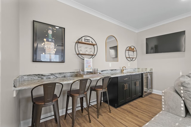 bar with baseboards, light wood-style flooring, wine cooler, ornamental molding, and a sink