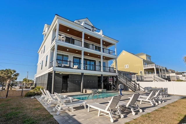 rear view of house featuring a patio, a balcony, stairway, a community pool, and fence