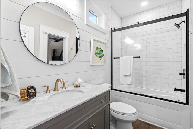 bathroom with wood finished floors, vanity, toilet, and bath / shower combo with glass door