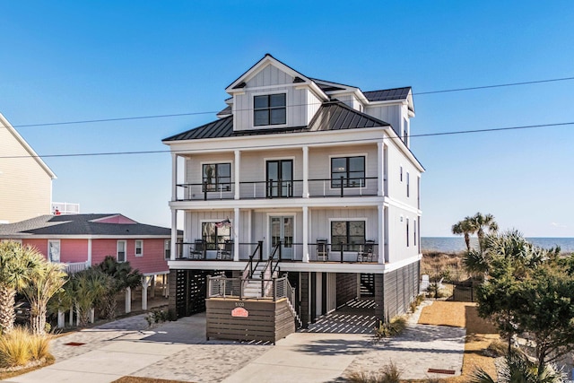 coastal inspired home with a porch, concrete driveway, board and batten siding, a standing seam roof, and a balcony