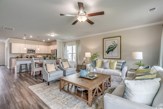 living area with dark wood-style floors, visible vents, ceiling fan, and ornamental molding