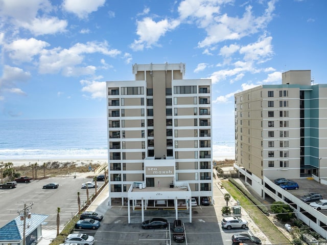 view of building exterior with a water view, uncovered parking, and a beach view