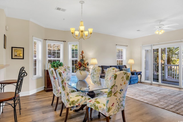 dining room featuring visible vents, ornamental molding, ceiling fan with notable chandelier, wood finished floors, and baseboards