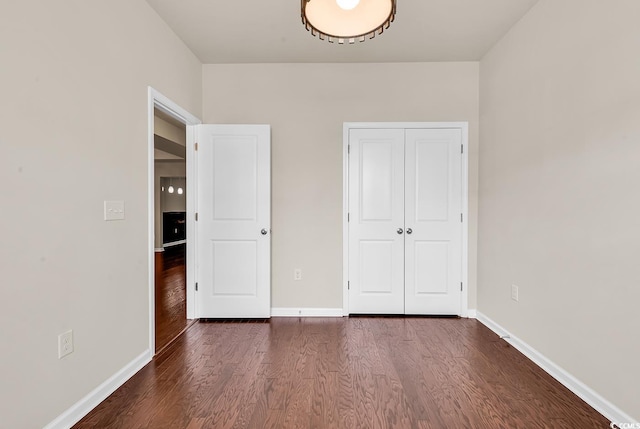 unfurnished bedroom with a closet, dark wood-style flooring, and baseboards