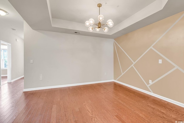 unfurnished room featuring a notable chandelier, wood finished floors, a raised ceiling, and baseboards