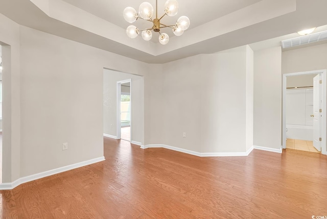 empty room featuring light wood-style floors, baseboards, visible vents, and a raised ceiling