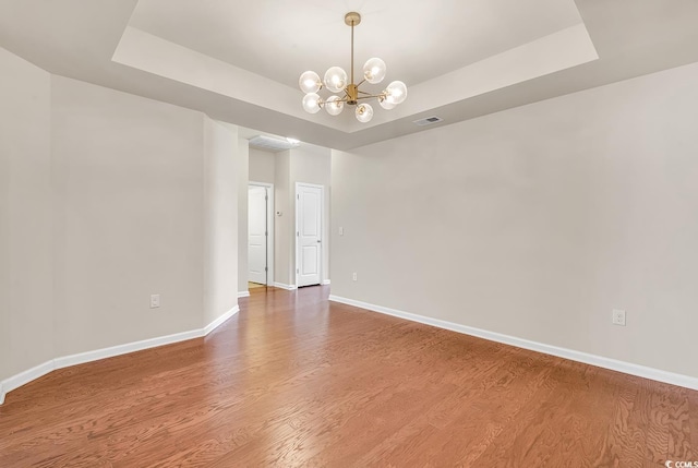 unfurnished room with a raised ceiling, visible vents, wood finished floors, a chandelier, and baseboards