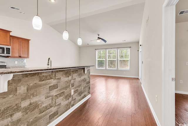 kitchen with visible vents, brown cabinets, hardwood / wood-style floors, vaulted ceiling, and stainless steel appliances