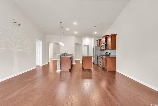 kitchen featuring appliances with stainless steel finishes, brown cabinetry, dark wood-type flooring, a sink, and baseboards