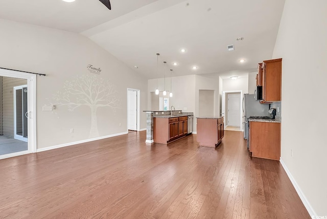 kitchen with dark wood-style floors, brown cabinetry, appliances with stainless steel finishes, a sink, and an island with sink