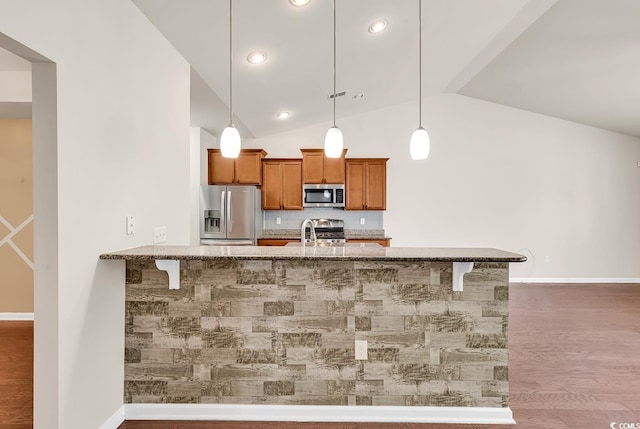 kitchen featuring brown cabinetry, appliances with stainless steel finishes, light stone counters, wood finished floors, and a sink