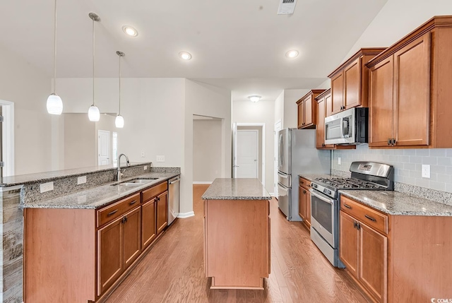 kitchen with light wood finished floors, stone countertops, appliances with stainless steel finishes, a peninsula, and a sink