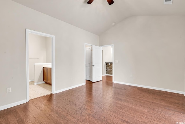 unfurnished bedroom with visible vents, baseboards, lofted ceiling, ensuite bath, and wood finished floors