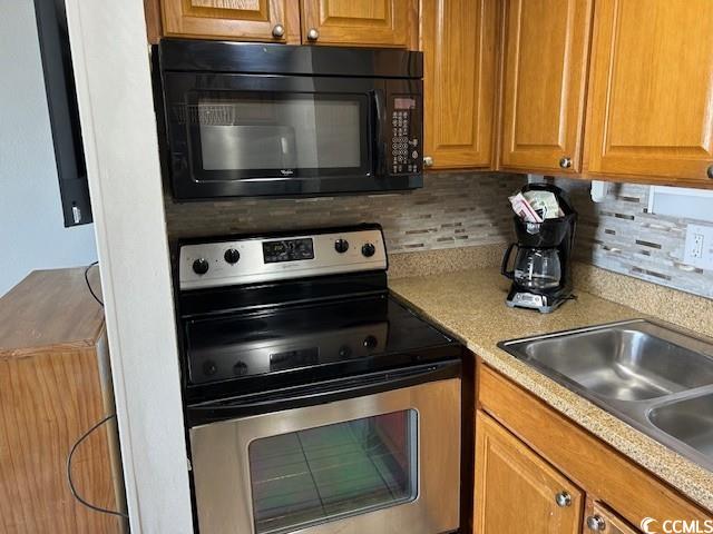 kitchen with black microwave, stainless steel range with electric cooktop, light countertops, decorative backsplash, and brown cabinets