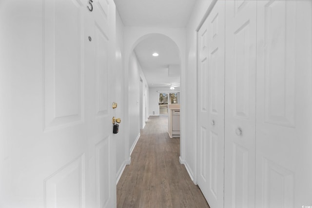 hall with baseboards, arched walkways, and dark wood finished floors