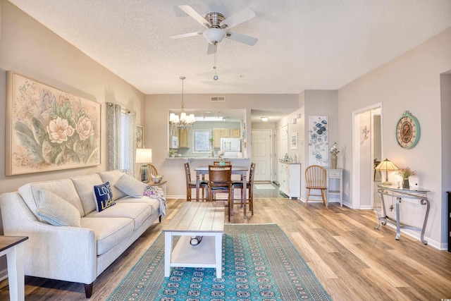 living area with baseboards, visible vents, light wood finished floors, a textured ceiling, and ceiling fan with notable chandelier