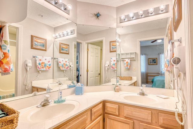 bathroom with a sink, a textured ceiling, ensuite bath, and double vanity