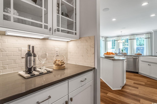 kitchen with dark countertops, wood finished floors, white cabinets, glass insert cabinets, and dishwasher