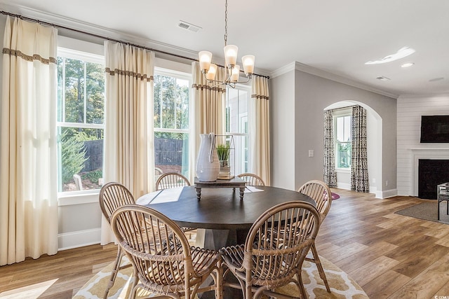 dining space featuring arched walkways, light wood-style flooring, a wealth of natural light, and ornamental molding