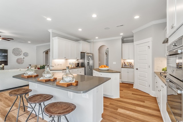 kitchen with a kitchen island, arched walkways, open floor plan, light wood-style floors, and stainless steel fridge