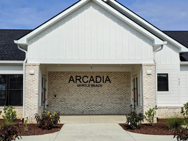 doorway to property with driveway, brick siding, board and batten siding, and roof with shingles