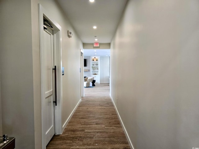 corridor with dark wood finished floors, built in features, recessed lighting, and baseboards