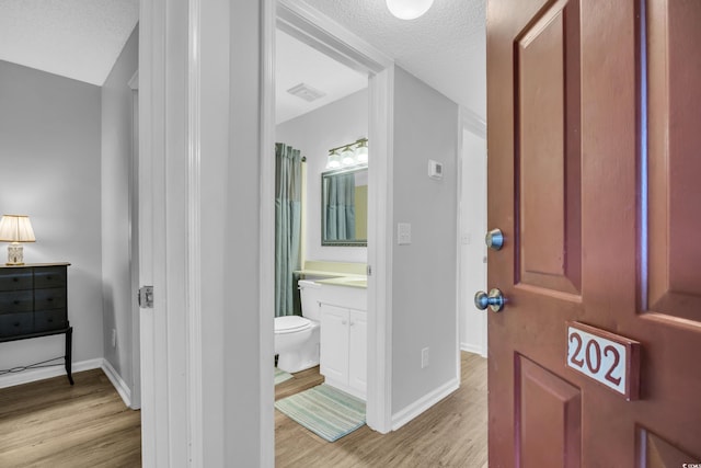 full bath with vanity, wood finished floors, visible vents, a textured ceiling, and toilet