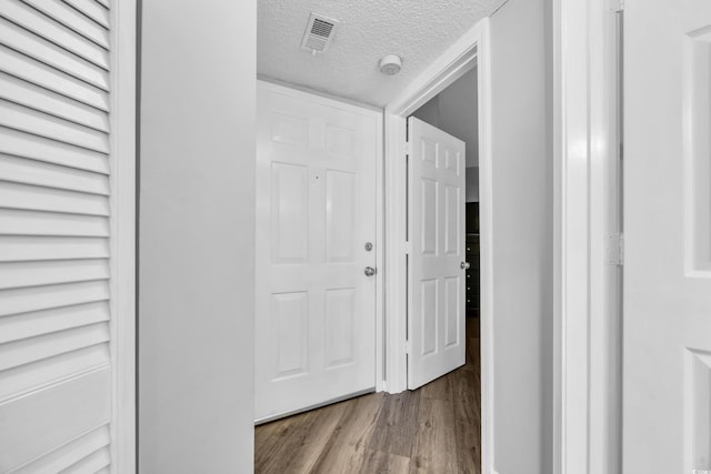 hallway featuring wood finished floors, visible vents, and a textured ceiling