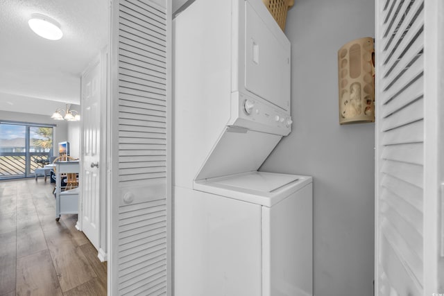 washroom with a notable chandelier, stacked washer and dryer, wood finished floors, and laundry area