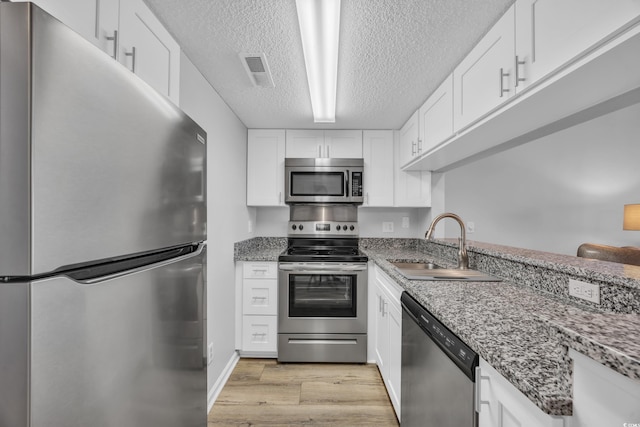 kitchen featuring visible vents, light wood-style flooring, a sink, white cabinets, and appliances with stainless steel finishes