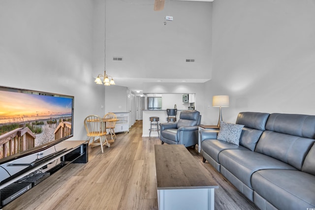 living area featuring visible vents, light wood-style floors, a towering ceiling, and a notable chandelier