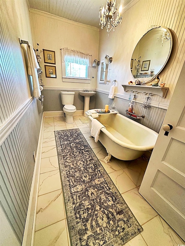 bathroom featuring toilet, marble finish floor, crown molding, and a wainscoted wall