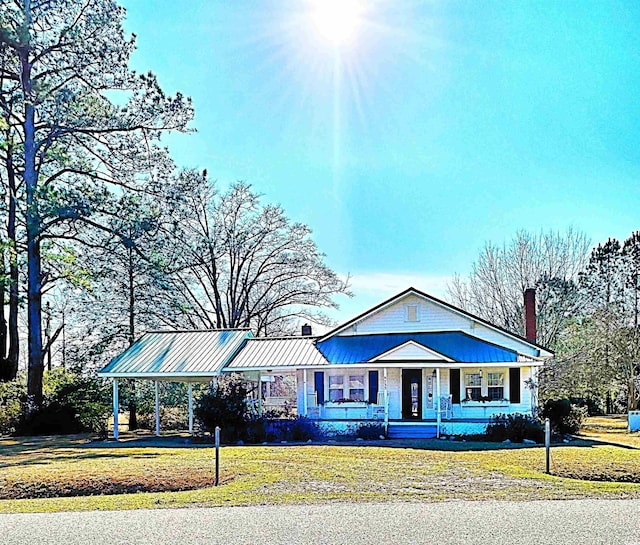 view of front of property featuring a standing seam roof, metal roof, covered porch, a chimney, and a front yard