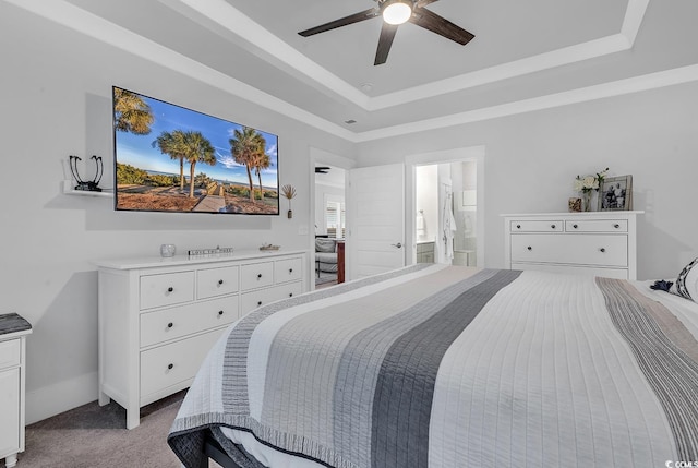 carpeted bedroom featuring a tray ceiling, a ceiling fan, baseboards, and ensuite bathroom